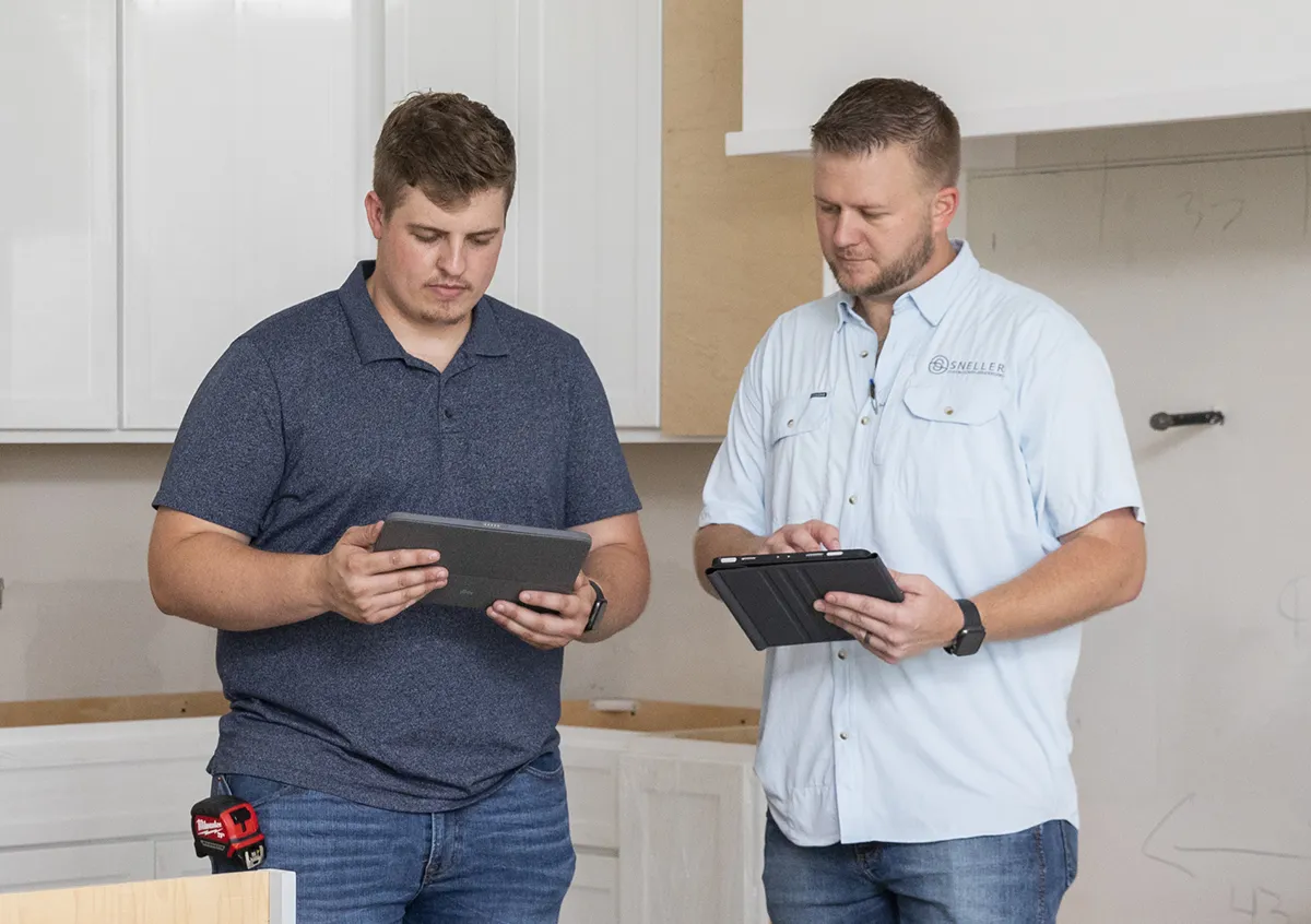 Two construction professionals reviewing project details on tablets inside a partially finished home interior.